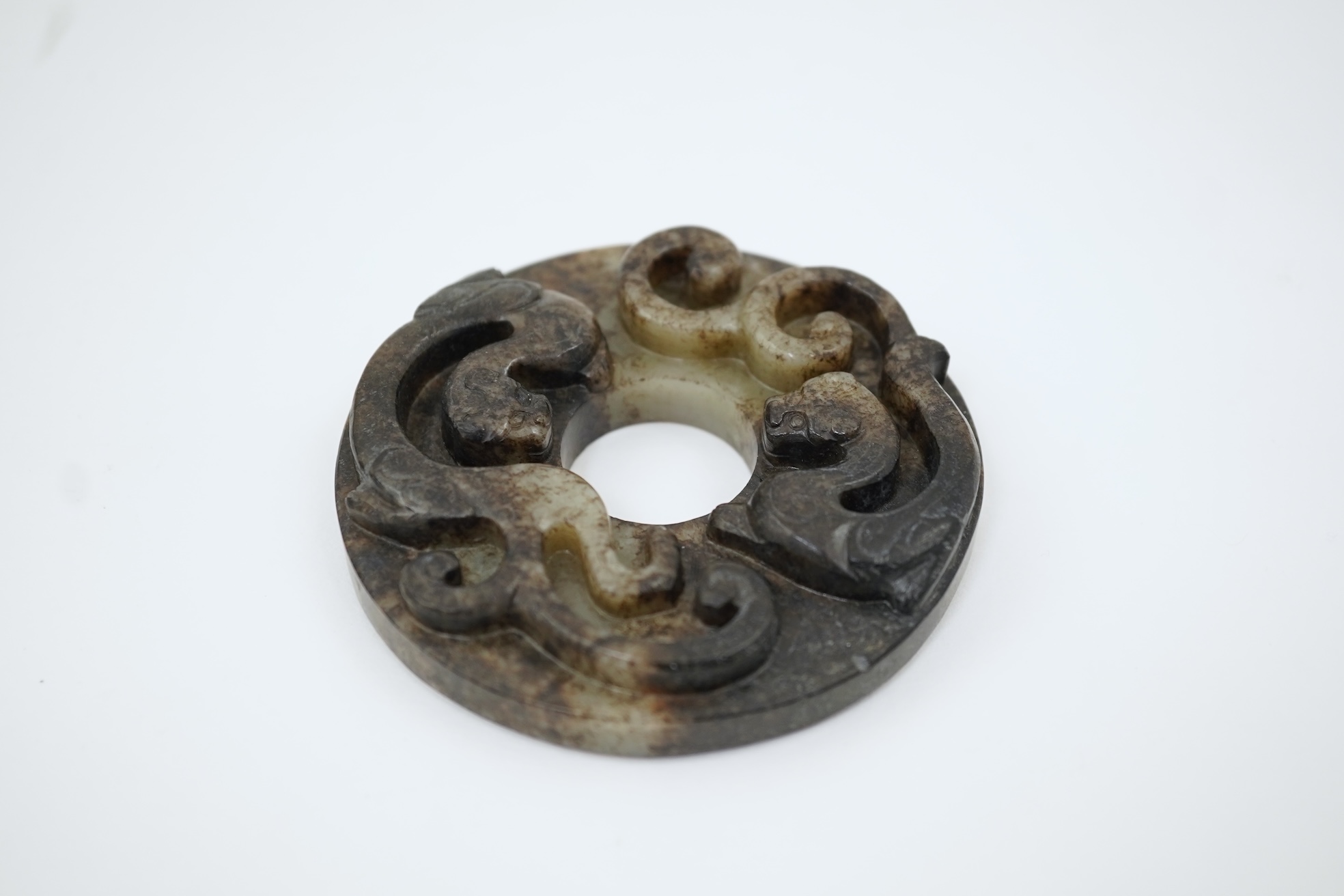 A Chinese pale celadon and black jade bi disc